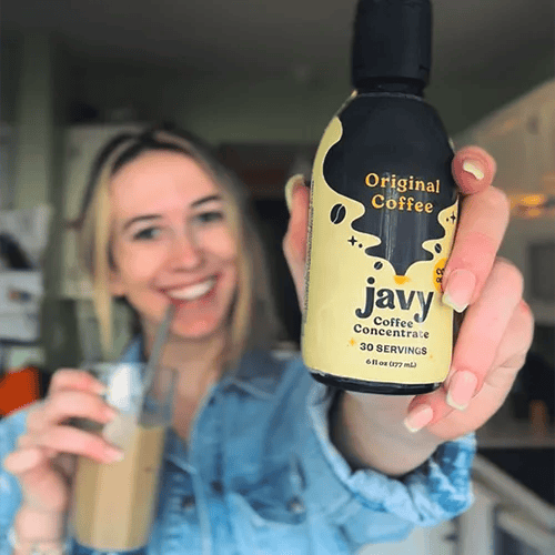 Woman holding Javy coffee concentrate bottle, smiling, and holding a glass of iced coffee.